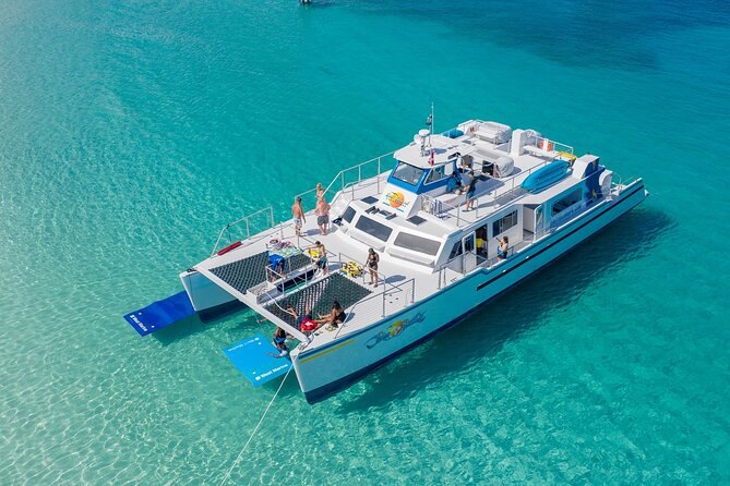 A large catamaran anchored over pale sand in turquoise water, seen from above