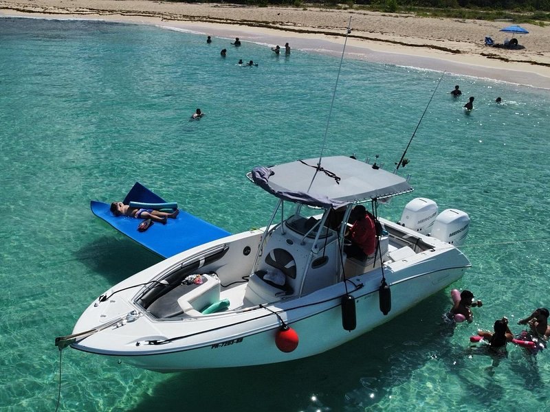 A centre-console boat anchored in shallow turquoise water, a floating mat and snorkelers beside it