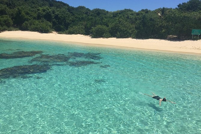 A sheltered cove with clear shallow water, a white beach and a green hillside