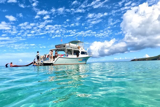 A snorkel boat anchored in calm turquoise water, a swimmer on a float behind it