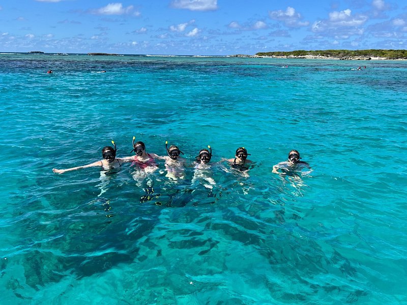 Snorkelers floating in a loose line over clear turquoise shallows