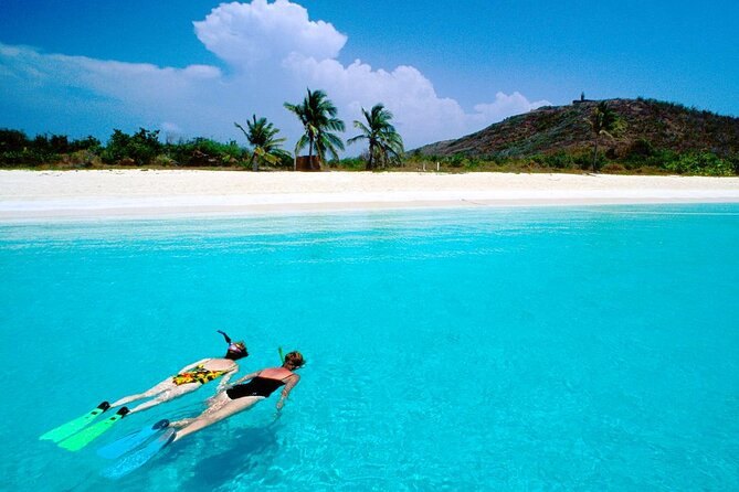Two snorkelers face down in turquoise water off a white-sand beach with palms