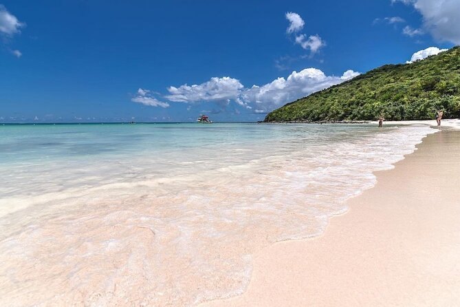 An empty white-sand beach curving into clear turquoise water below a green headland
