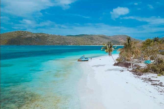 A white-sand spit with palm trees and turquoise water, a green island across the channel
